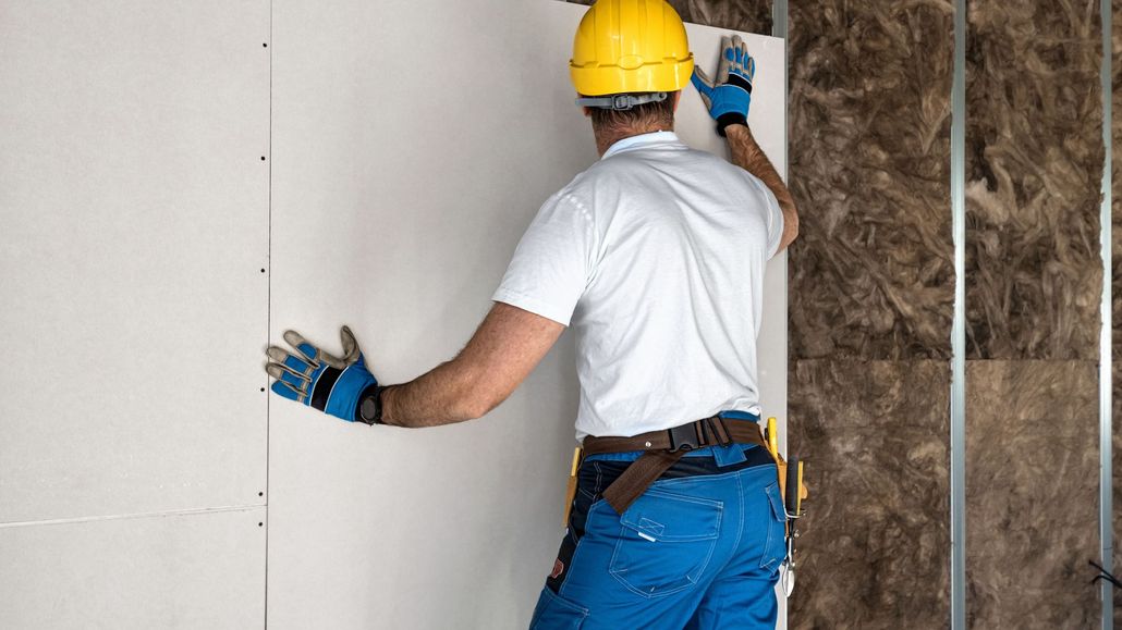 Worker in yellow hard hat installing insulation panels on a wall indoors