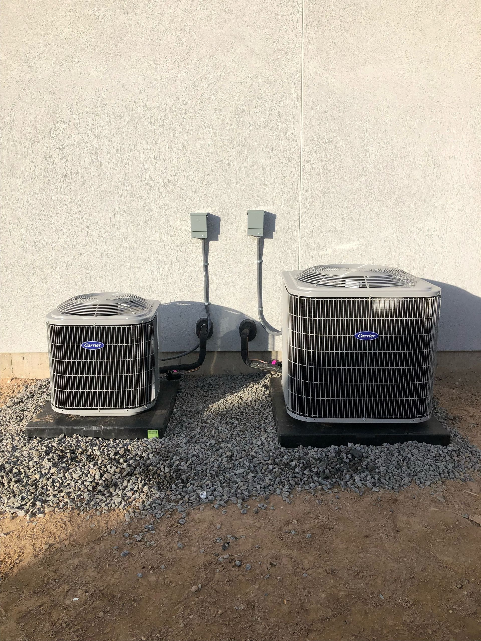 Two air conditioners sit on top of gravel in front of a building.