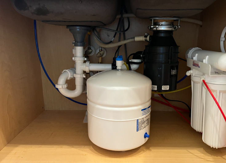 Under-sink water filtration system with white tanks, pipes, and a black filter unit in a cabinet