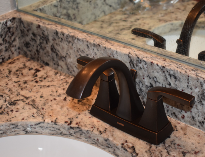 Dark bronze bathroom faucet on a speckled granite countertop beside a sink.