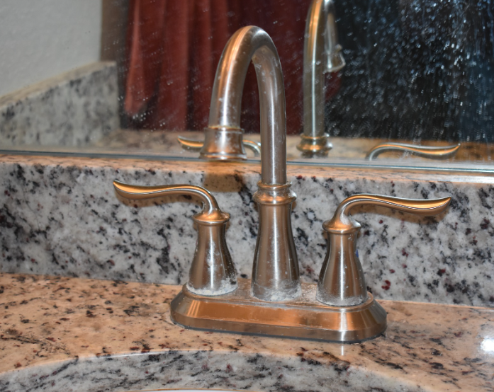 Chrome bathroom sink faucet on speckled granite countertop and backsplash