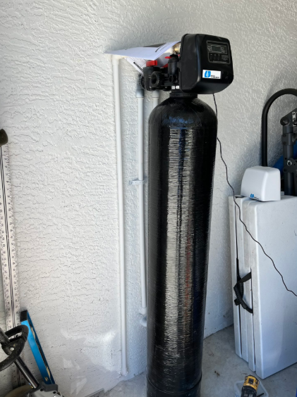 Tall black water softener tank with digital control head in a utility room, beside a white cabinet.
