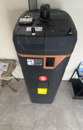 Black industrial machine with orange accents on a tiled floor indoors