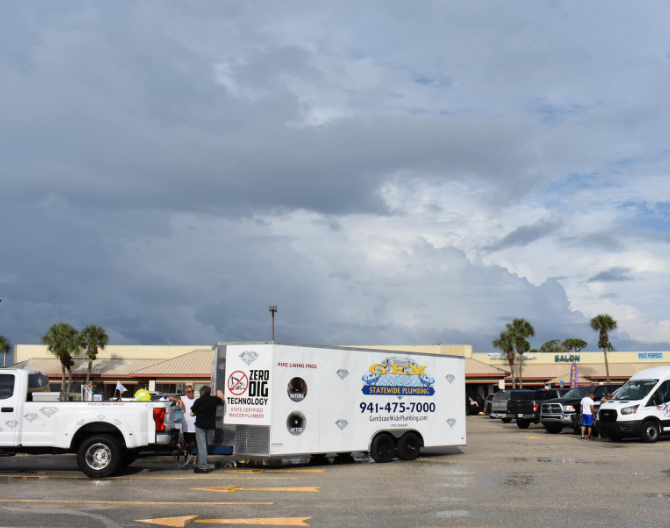 Parking lot with a white utility trailer and trucks under a cloudy sky outside a shopping center.