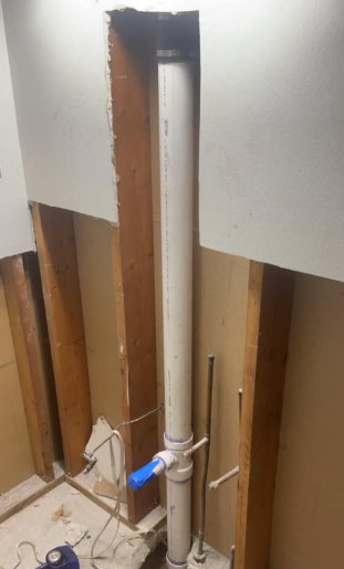 Partially torn drywall exposing pipes and wiring inside a wall cavity