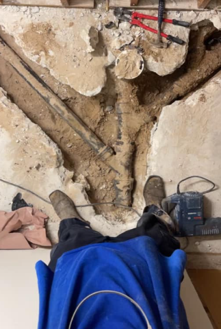 Archaeological excavation trench with exposed stone walls and tools, viewed from above.
