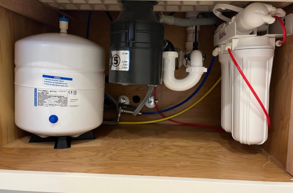 Under-sink water filtration system with white tank, black filter, and tubing in a cabinet