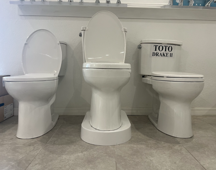 Three white toilets on display in a showroom, each with the lid up.