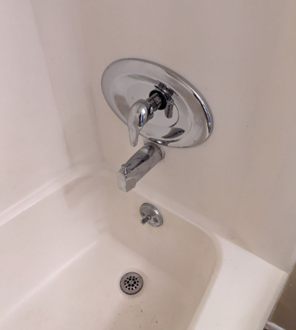 Chrome bathtub faucet and shower diverter over a white tub with drain