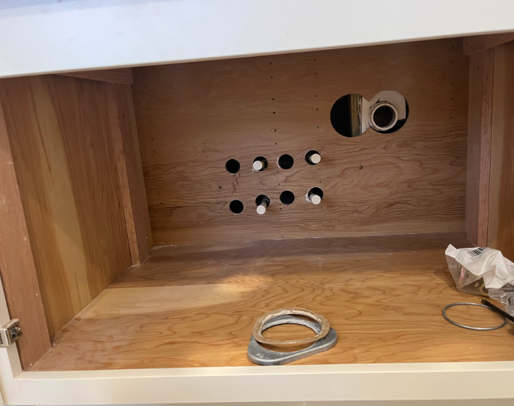 Wooden cabinet interior with drilled holes, outlet cutouts, and loose wires on the bottom.