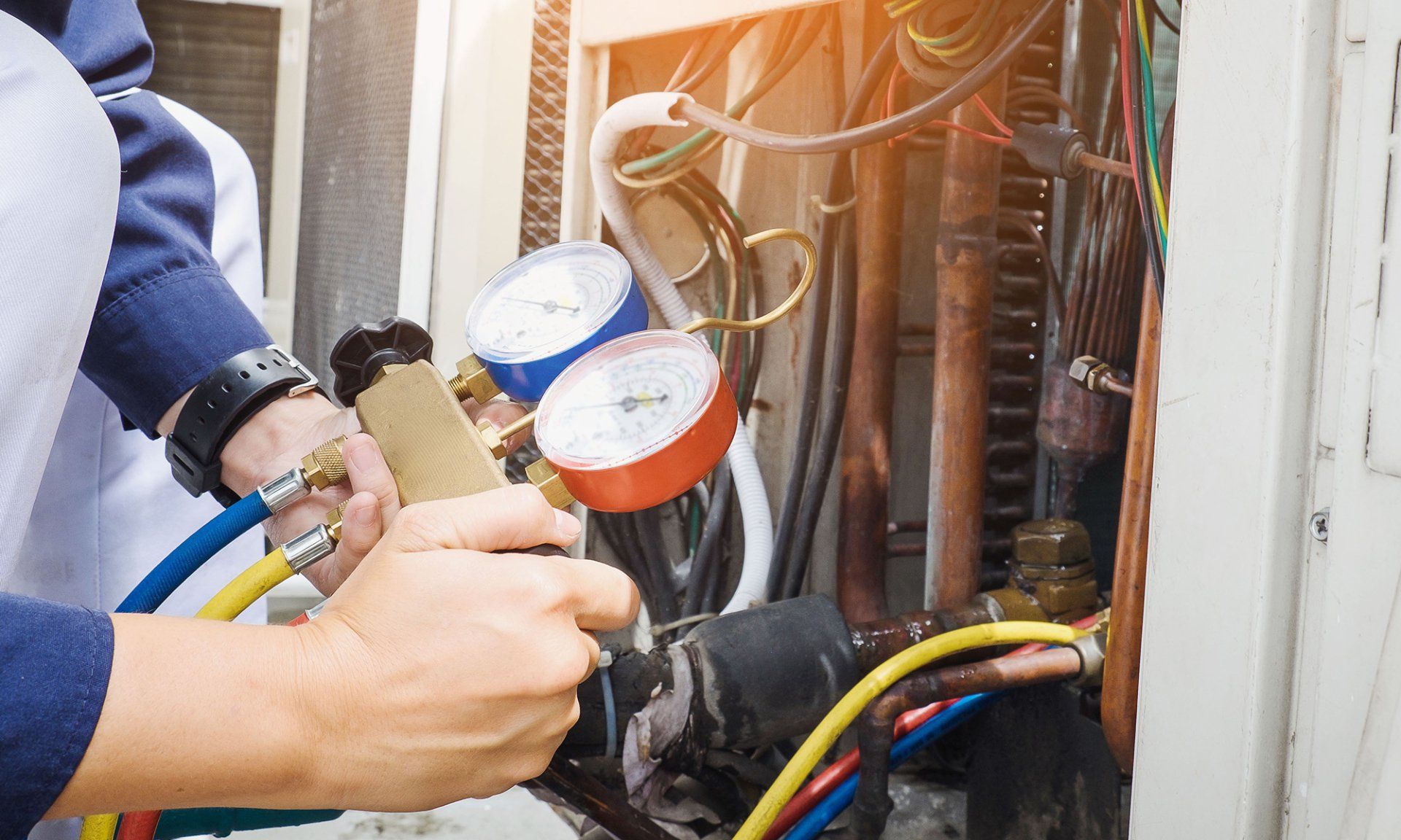 A man is working on an air conditioner with a pressure gauge.