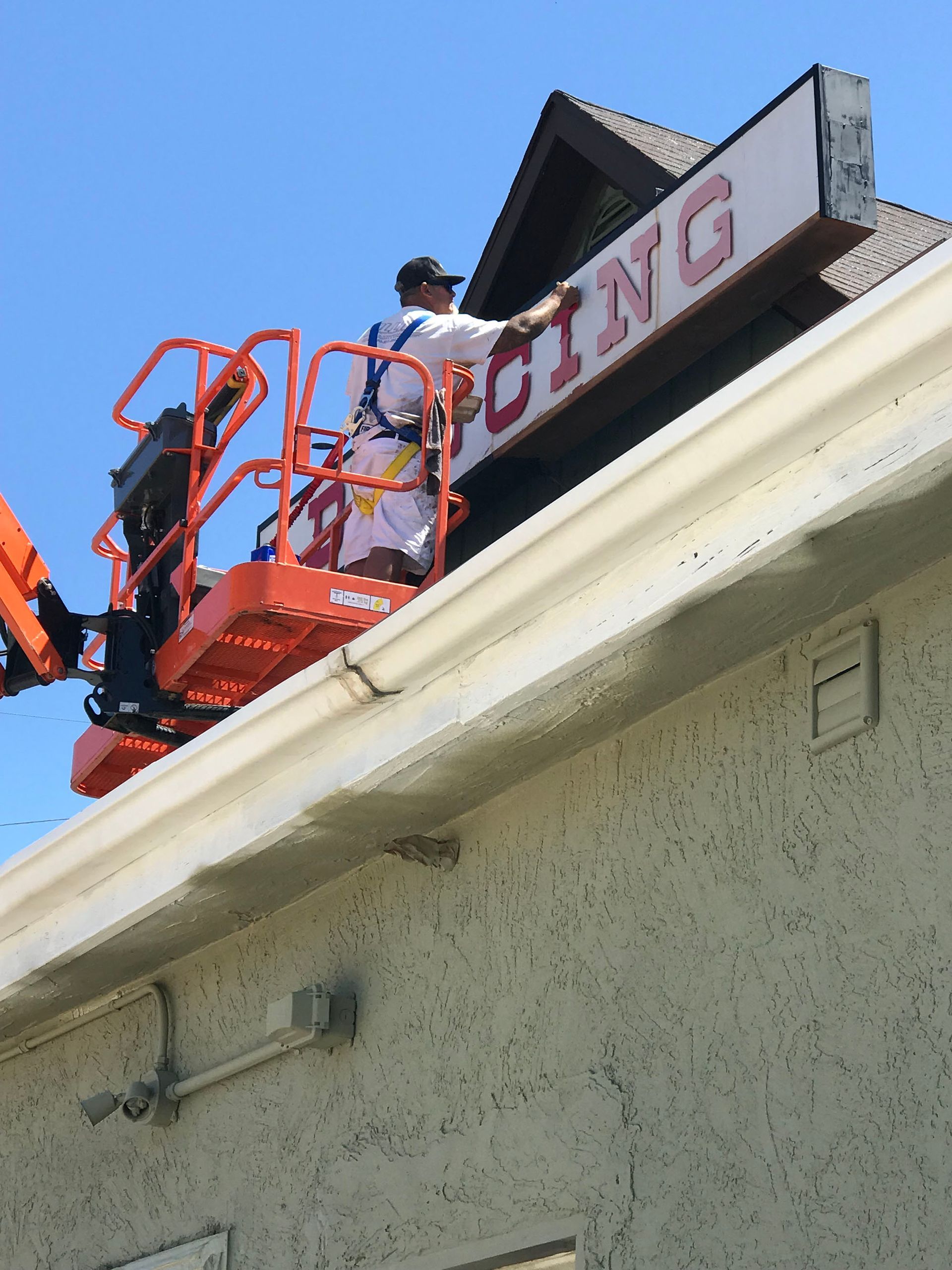 A man on a crane is working on a sign that says pricing