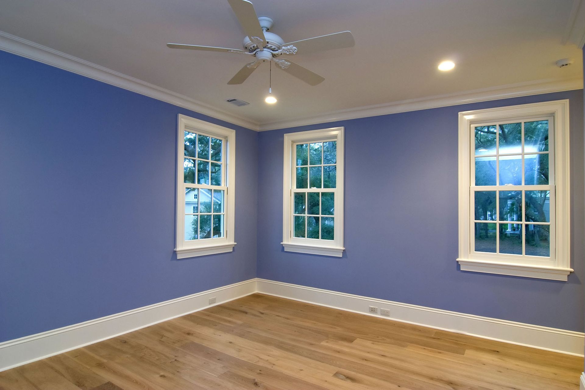 An empty room with a ceiling fan and three windows