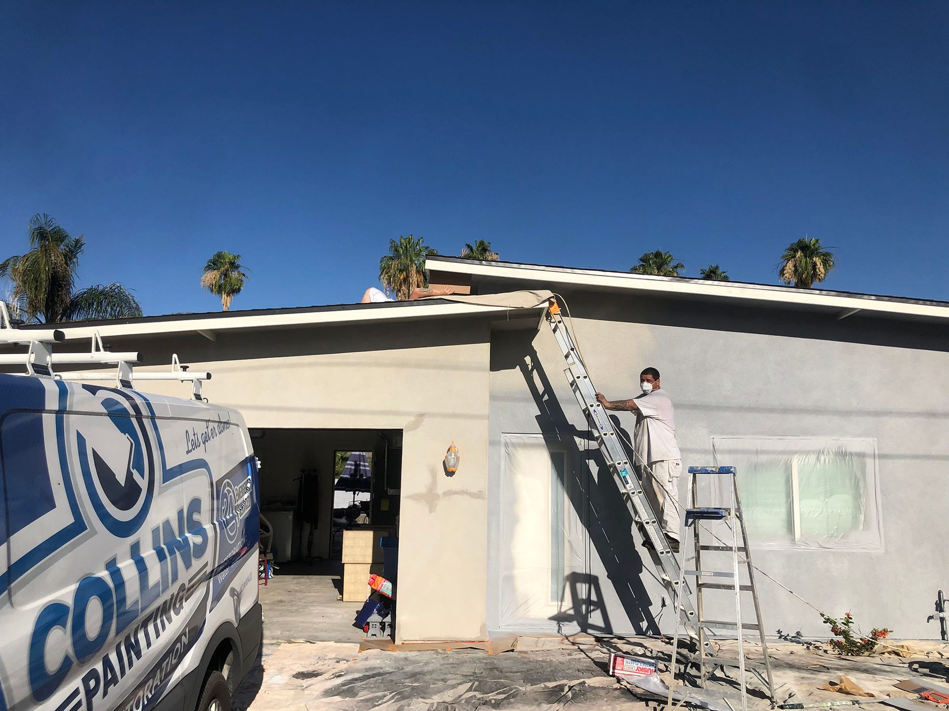 A man is painting the side of a house with a ladder.