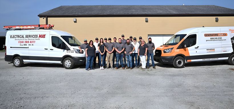 Group standing between two branded work vans in front of a warehouse building.