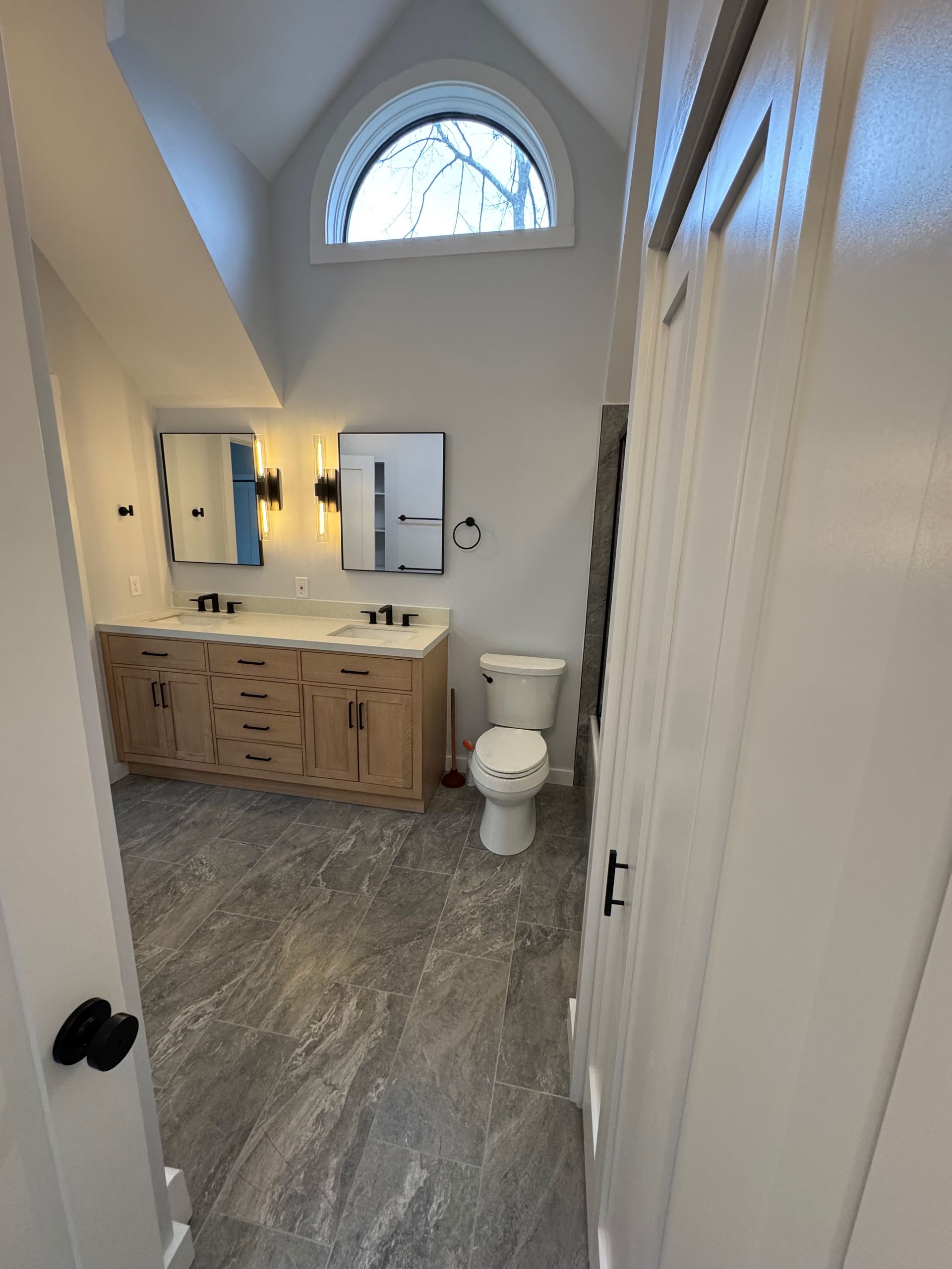 A bathroom with a toilet, sink, mirror, and window.