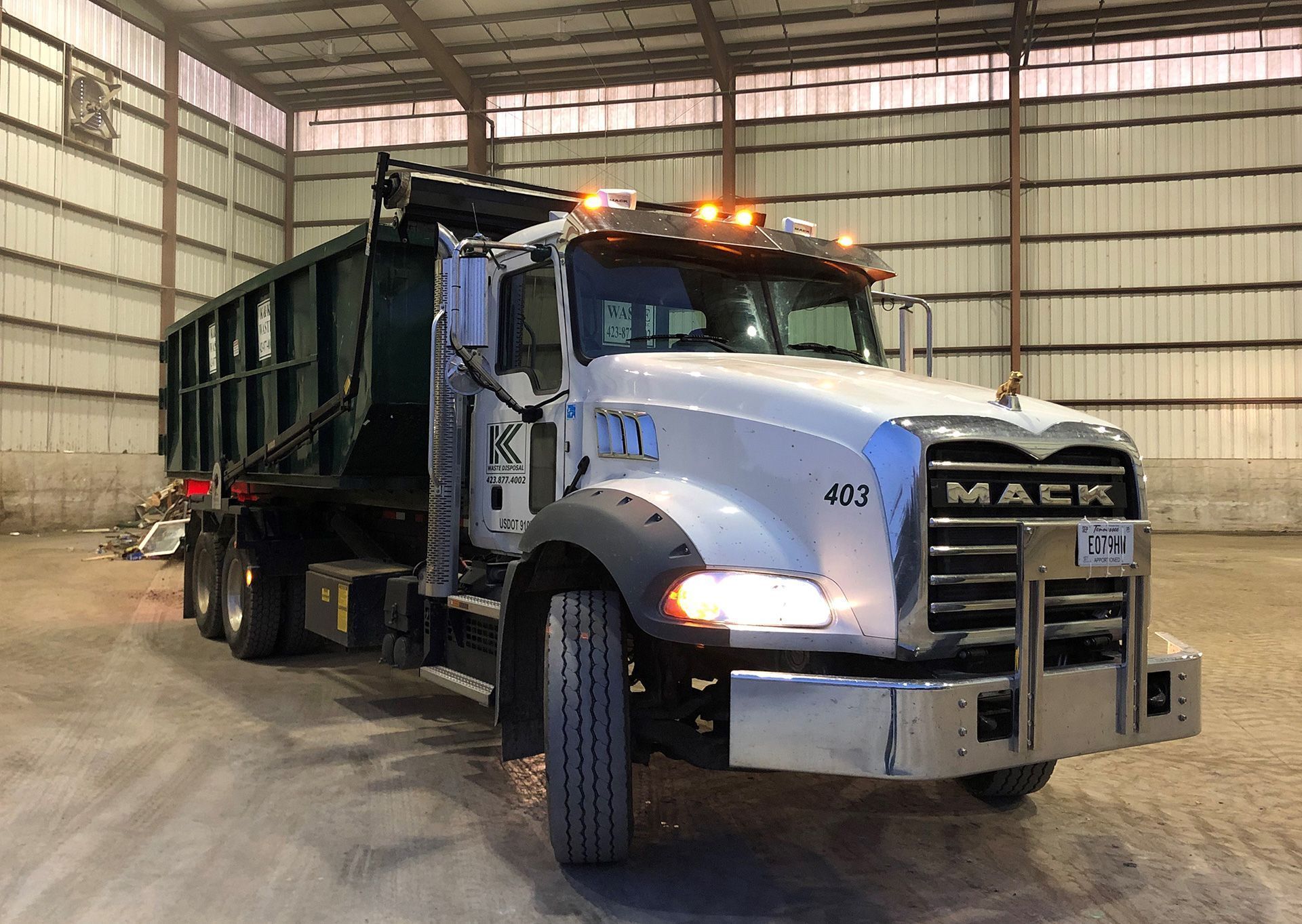 A white Mack dump truck parked inside a large, industrial warehouse with metal walls.