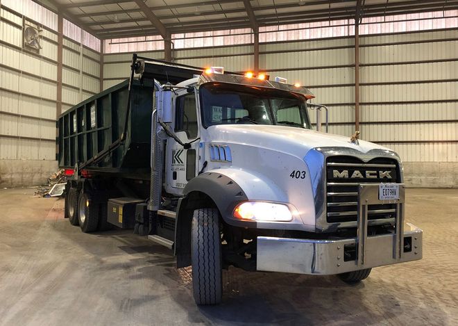 A white Mack dump truck parked inside a large, industrial warehouse with metal walls.