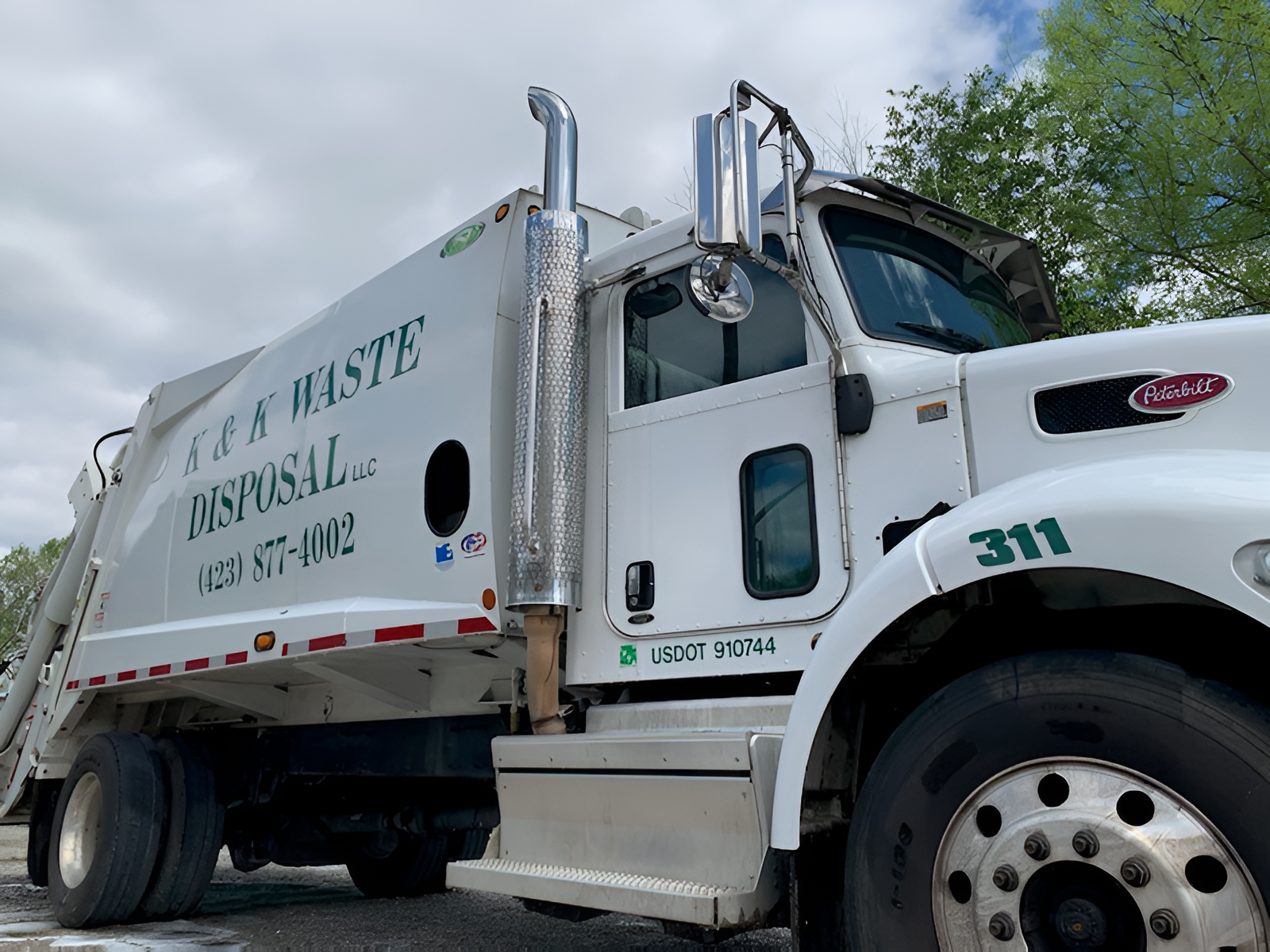 A white Peterbilt garbage truck labeled S&H Waste Disposal with the number 311 on its hood, parked outdoors.