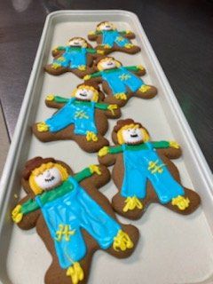 scarecrow cookies with blue overalls on a pan of other cookies
