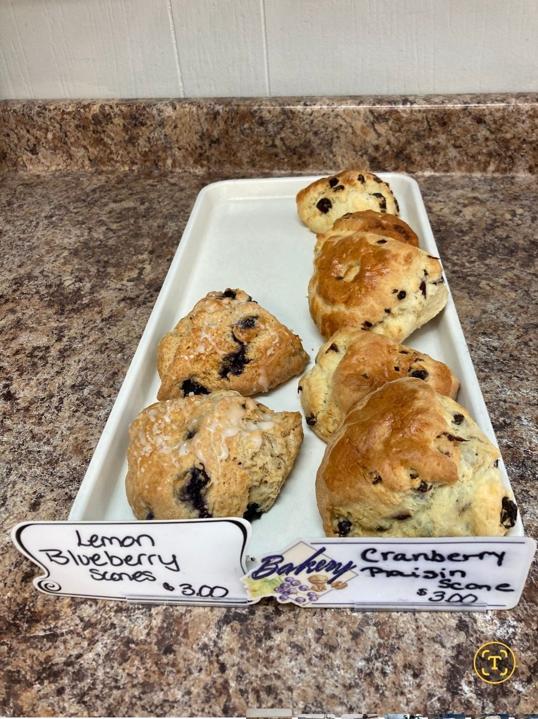 Assorted scones on a white tray with handwritten labels for lemon blueberry and cranberry orange flavors