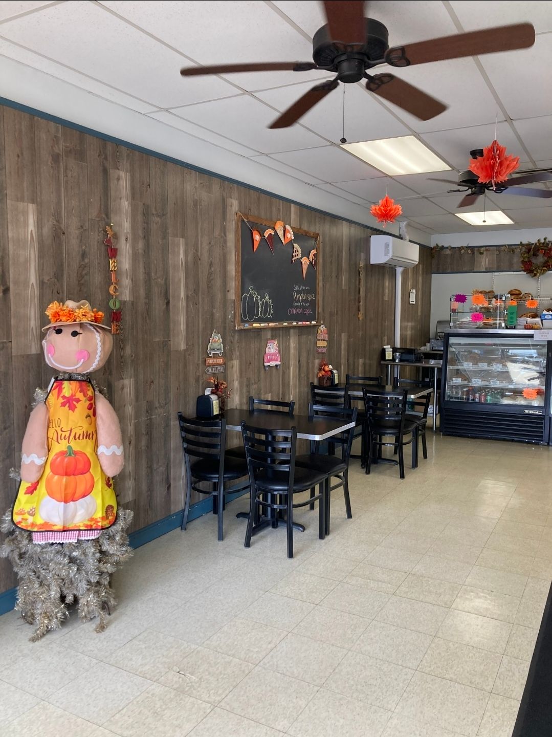 Cozy café interior with rustic wood walls, hanging lights, black tables, and a refrigerated display case.