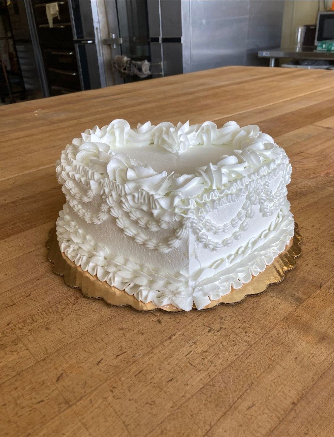 White heart-shaped cake with ornate frosting on a gold board on a wooden table
