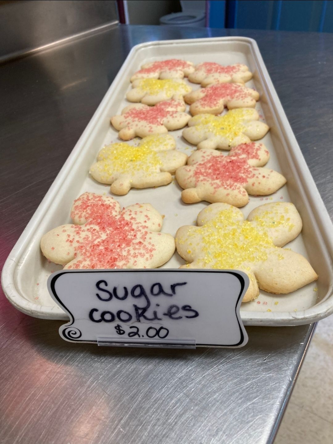 Tray of sugar cookies with pink and yellow sprinkles on a counter, labeled Sugar Cookies $4.00