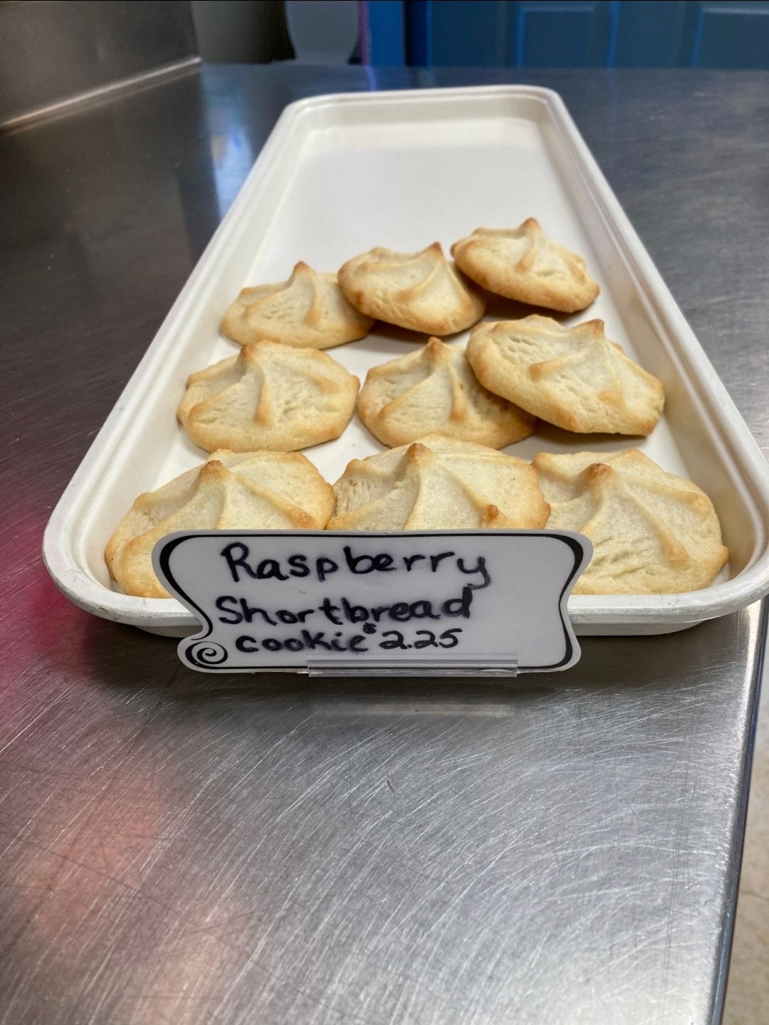 Tray of raspberry shortbread cookies with a label on a stainless steel counter.