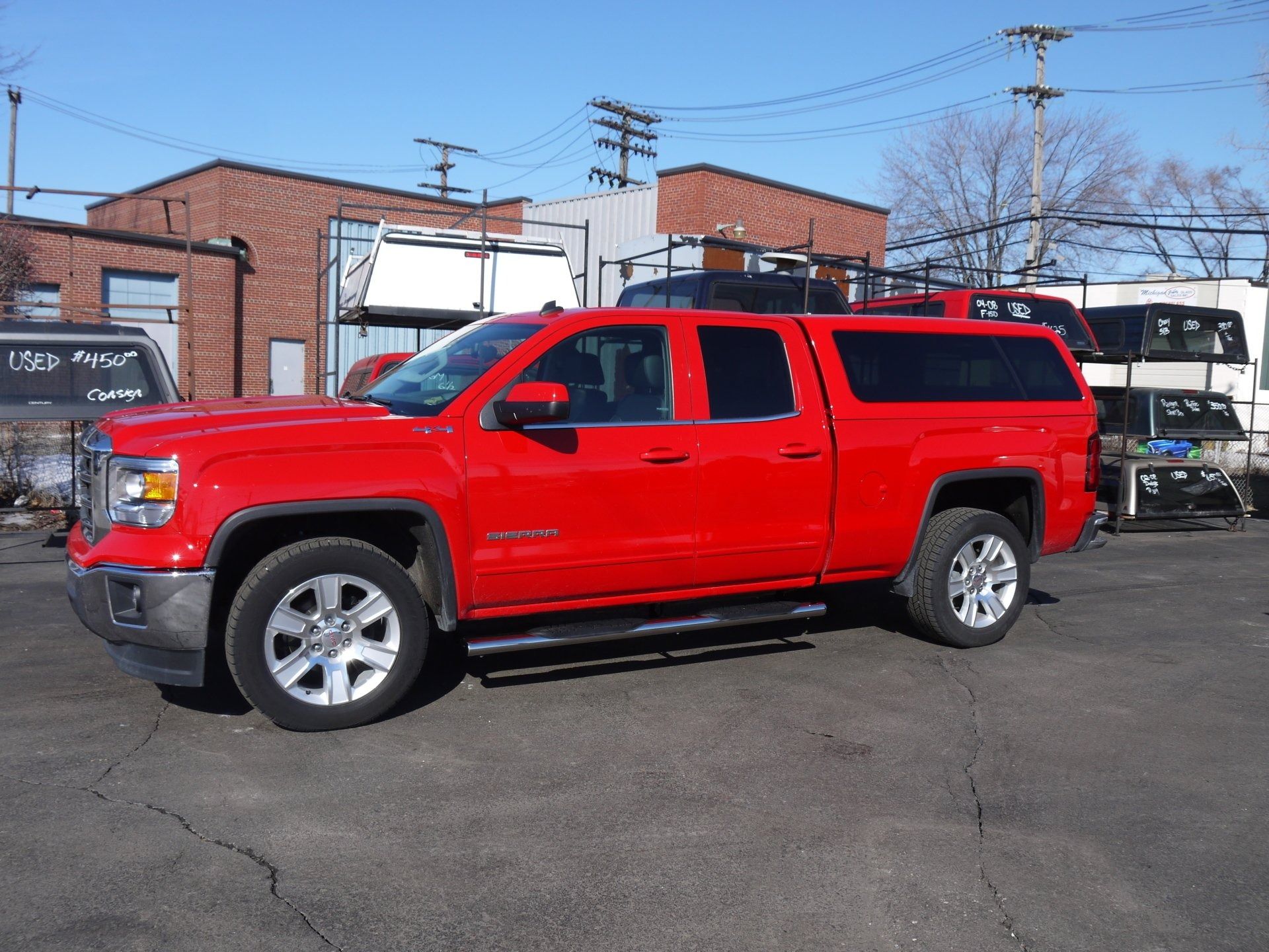 A bright red GMC pickup truck with a camper shell parked in an outdoor lot on a sunny day.