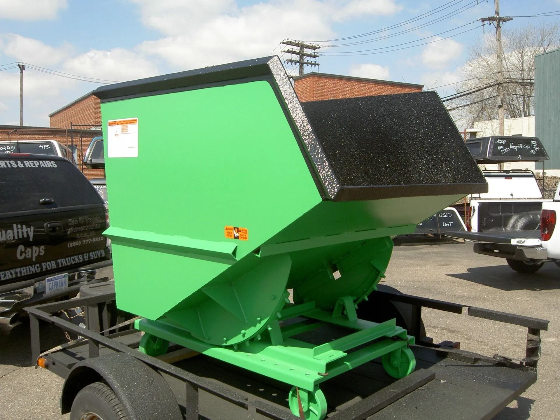 A bright green industrial self-dumping hopper sits mounted on a flatbed trailer outdoors on a sunny day.