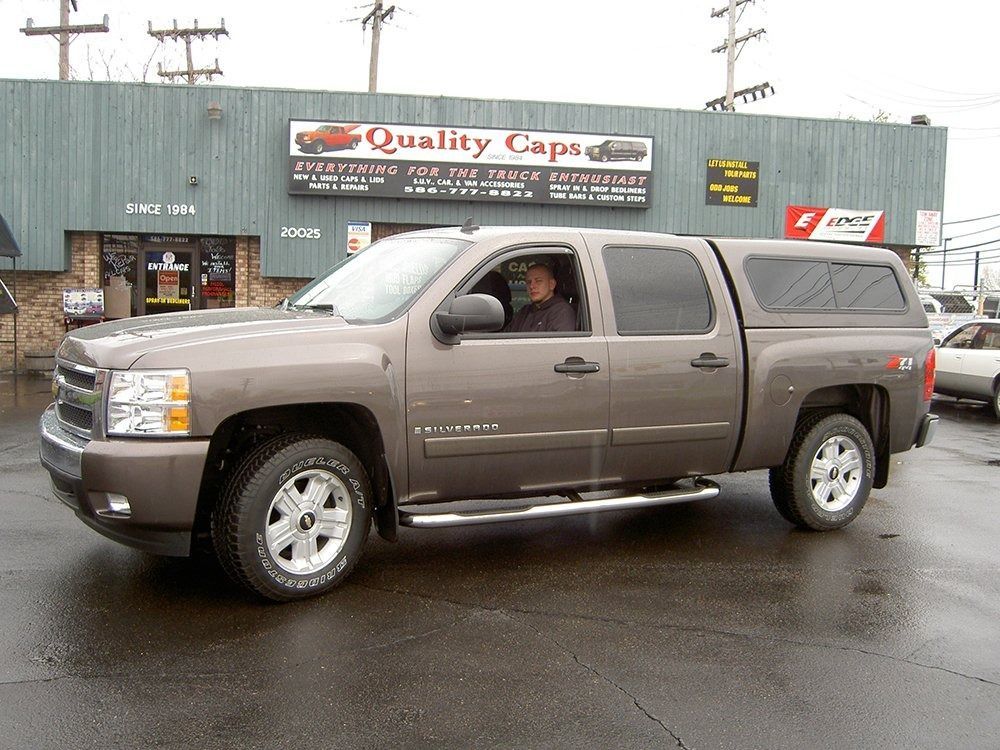 A bronze pickup truck with a camper shell parked in front of a building with a 