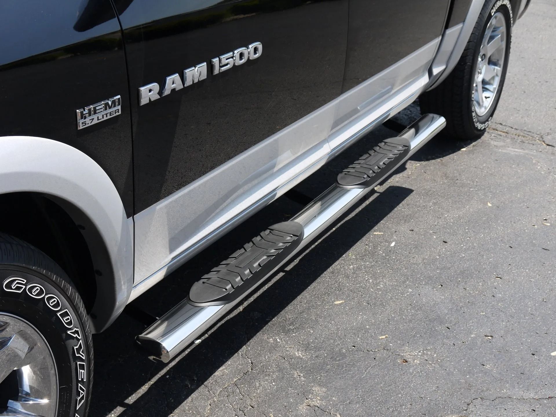 A close-up of the side of a black and silver Ram 1500 truck, focusing on the chrome side step running board.