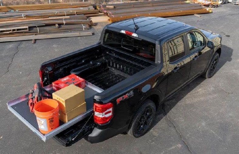 A black Ford Ranger FX4 pickup truck with an extended cargo bed slide holding a bucket, cardboard boxes, and red gear.