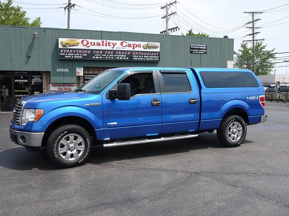 A bright blue Ford pickup truck with a matching truck cap parked in front of a Quality Caps storefront.