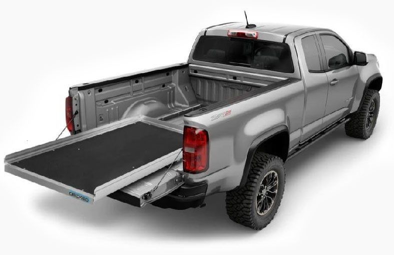 A silver pickup truck with a black cargo bed slide extended out over the lowered tailgate.