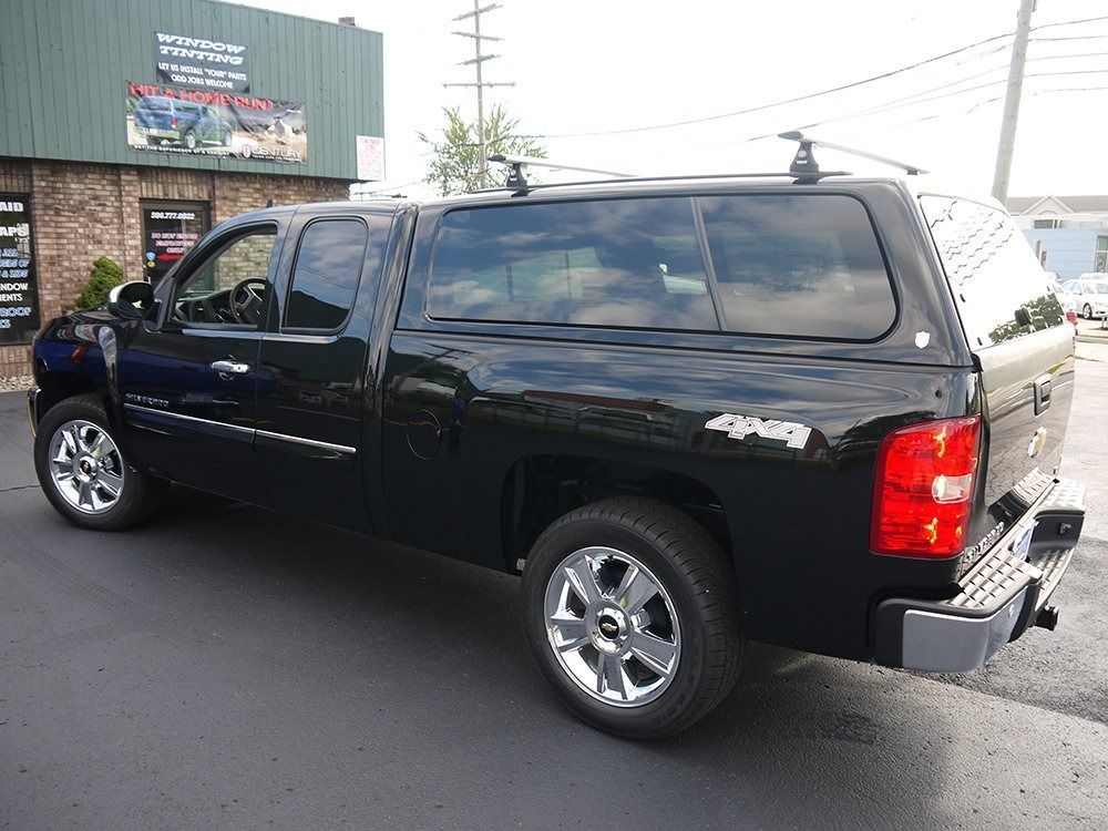 A black pickup truck with a camper shell parked in front of a brick building.