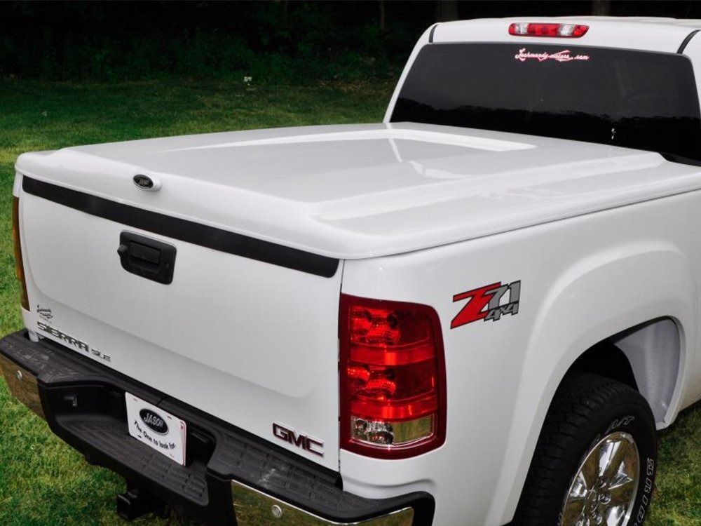 A white GMC pickup truck with a Z71 decal, featuring a smooth, hard-shell tonneau cover over the truck bed.