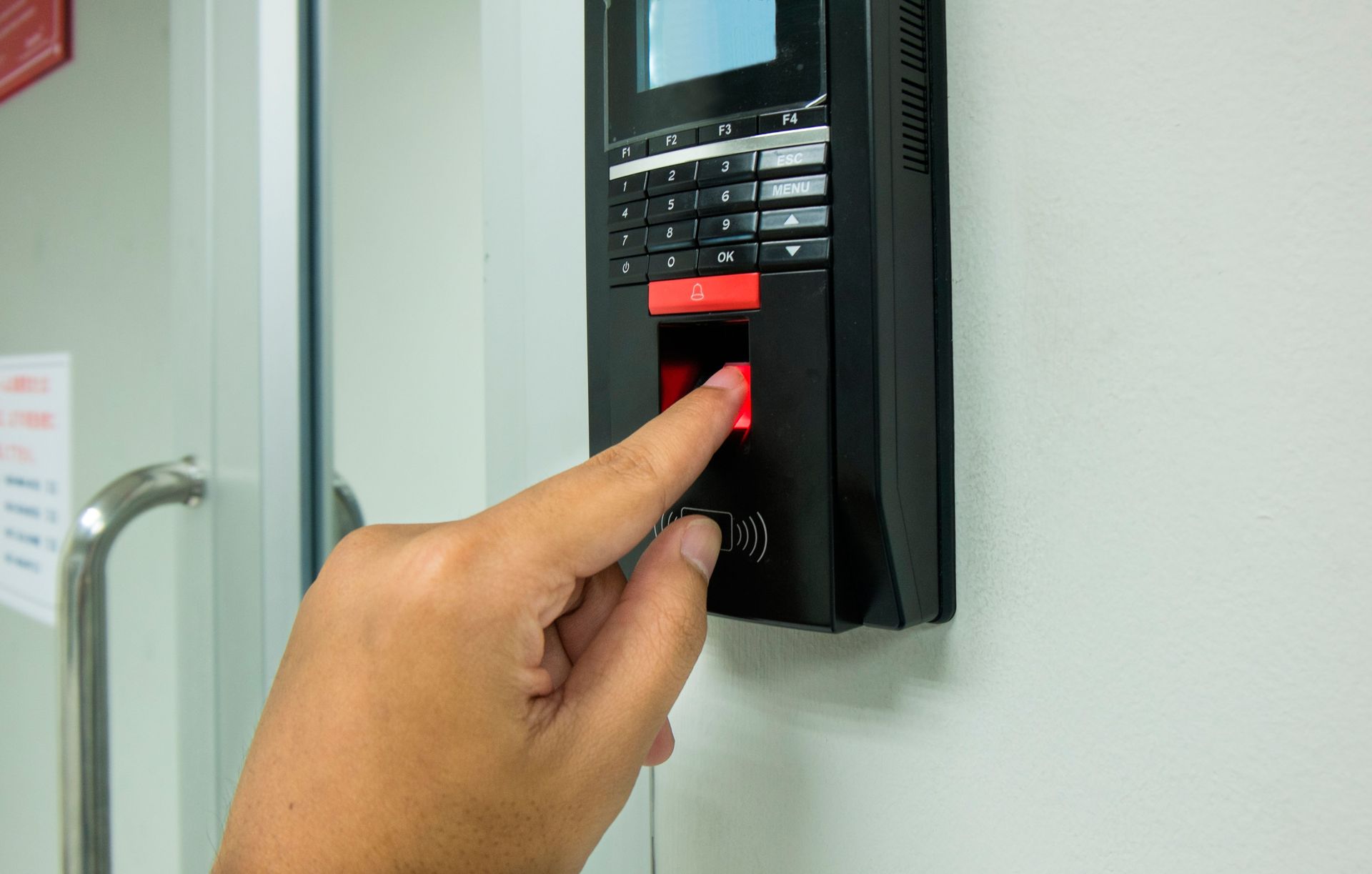 Person's finger scanning a fingerprint on a black security device mounted on a white wall.
