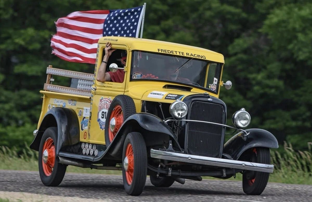 Yellow vintage pickup truck with American flag driving on a road