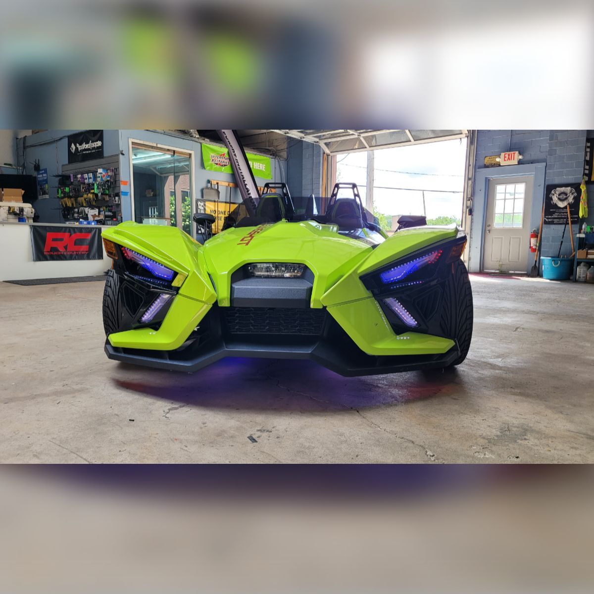 A neon green slingshot is parked in a garage