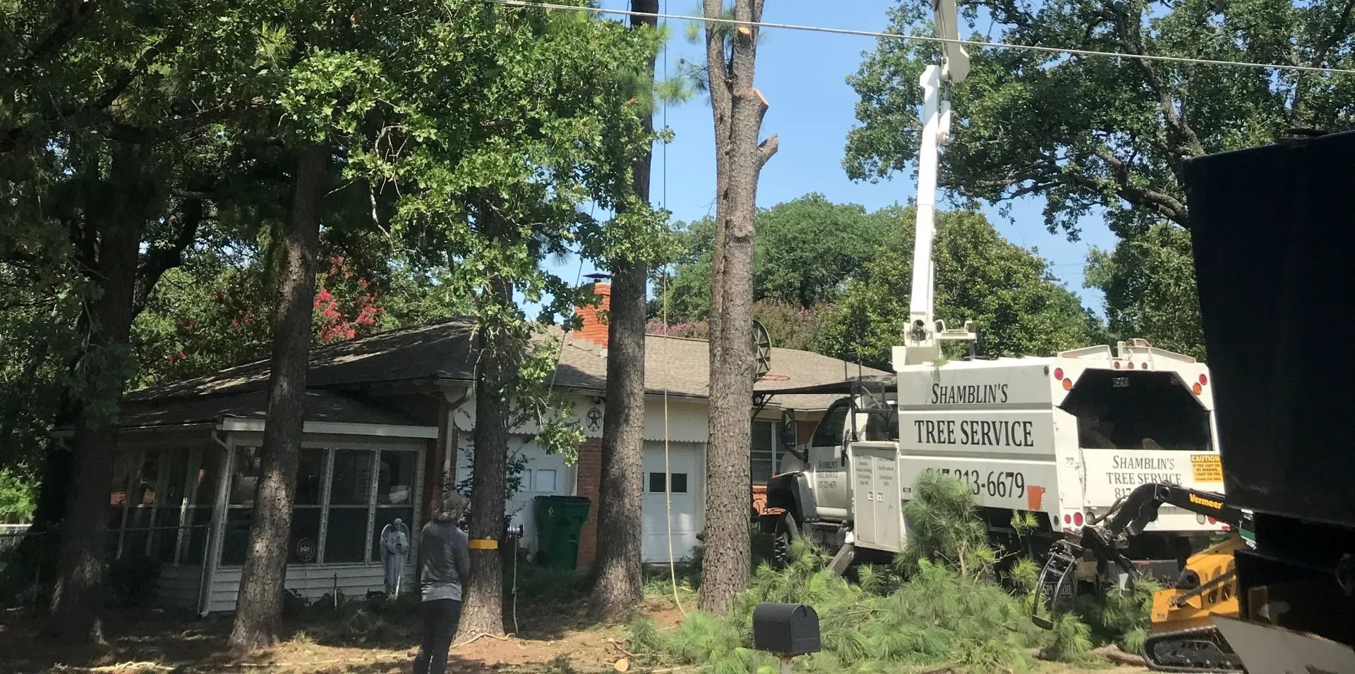 Tree service removing a tree in front of a house. A lift truck is used.