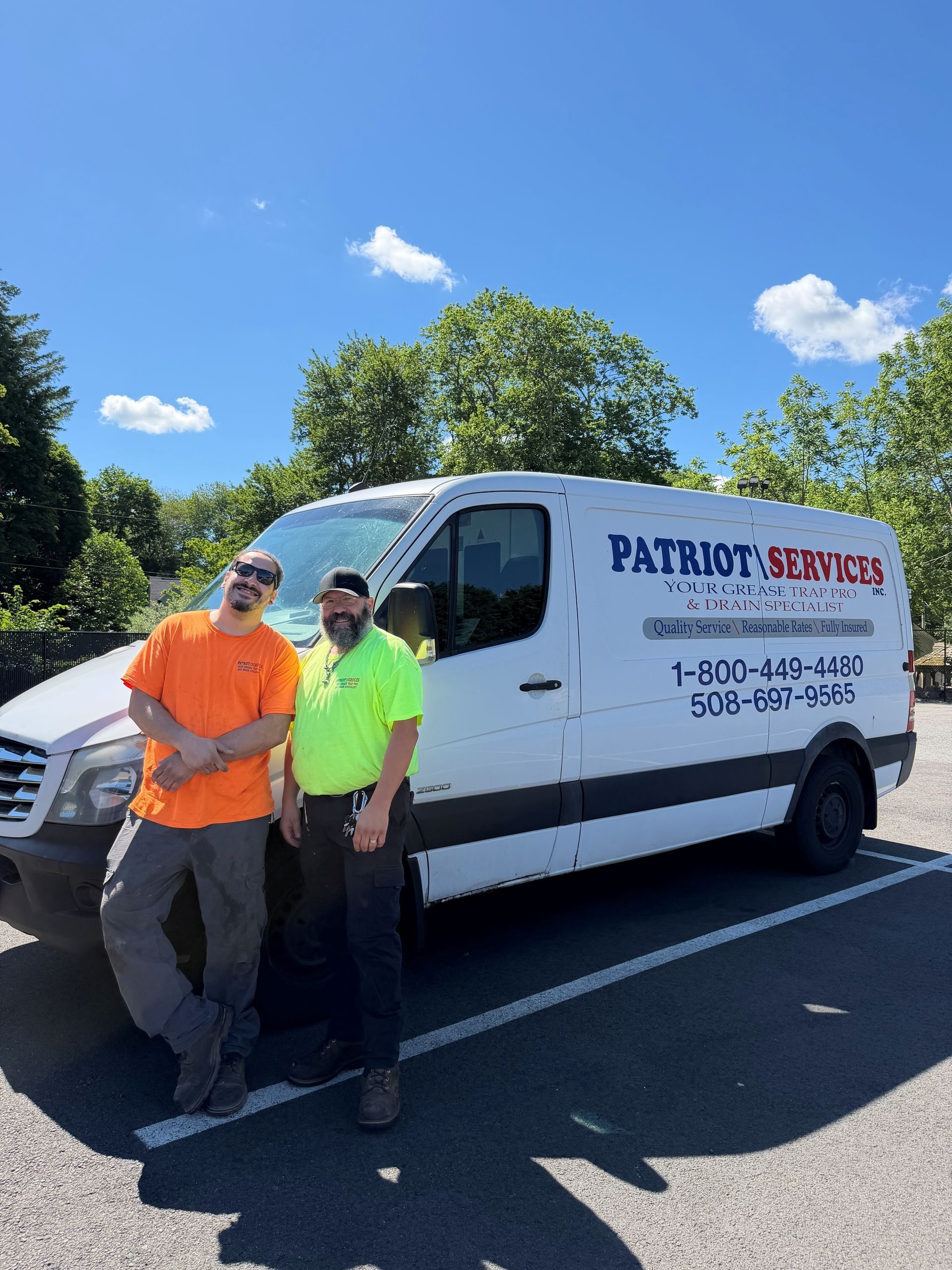 Two workers standing by a white Patriot Service van on a sunny roadside.