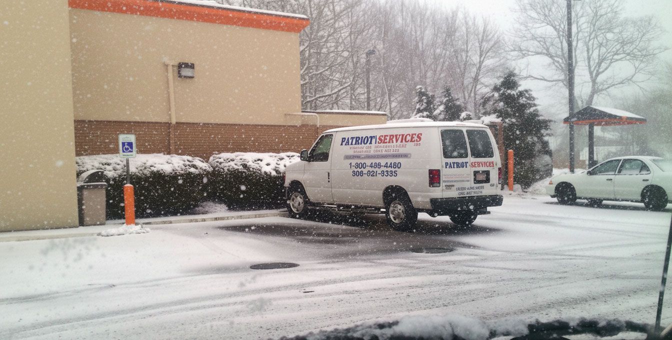 White van parked in a snowy parking lot next to a building, snow falling, cloudy day.