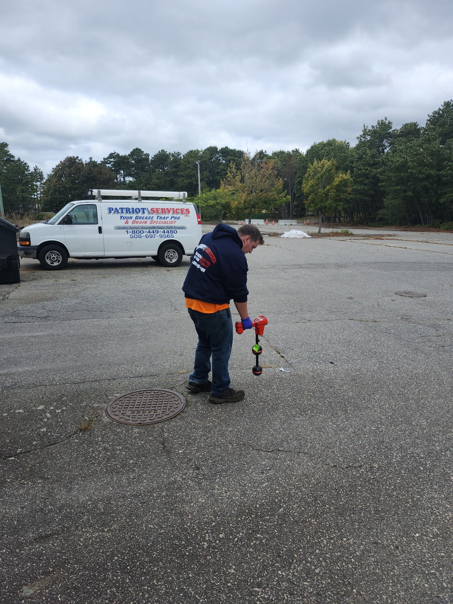 Man working on a sewer drain, truck in background. Outdoors, cloudy day.