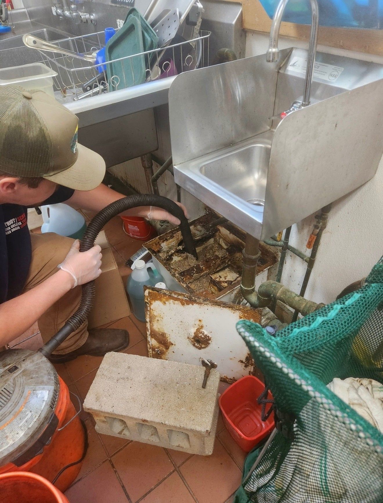 Person cleaning debris from a kitchen floor near a sink. Gray metal and orange accents are visible.