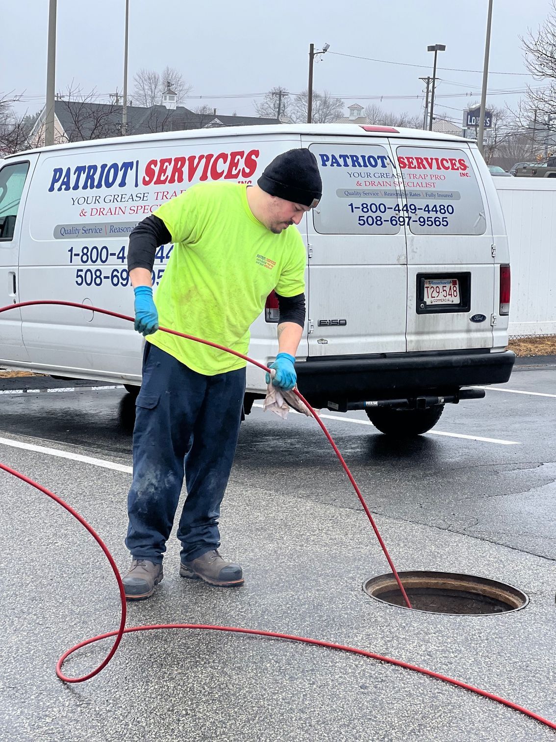 Man in neon green shirt uses a cable to inspect a manhole in a parking lot next to a Patriot Services van.