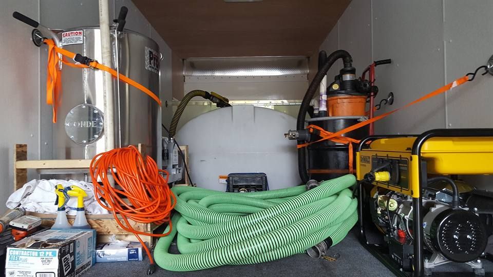Inside a trailer, pressure washing equipment is secured with straps, including a water tank, hoses, and a generator.