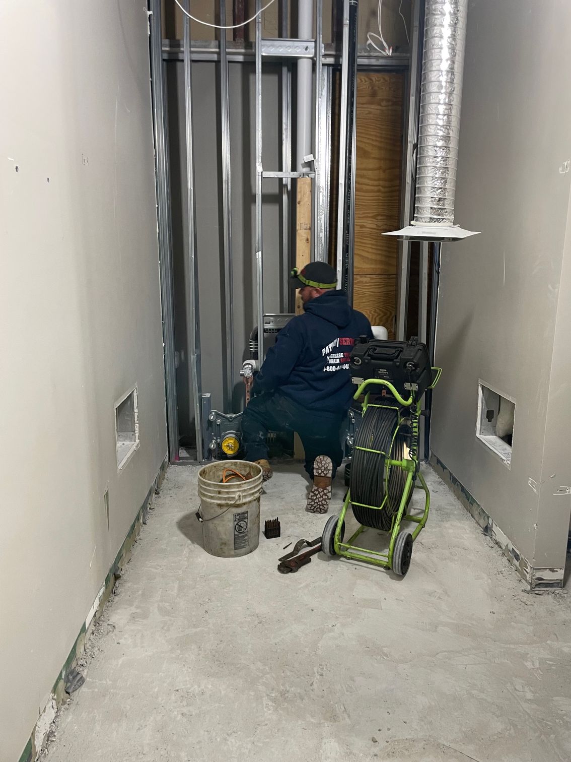 A person in a construction zone is working with equipment. The area has metal studs and concrete flooring.