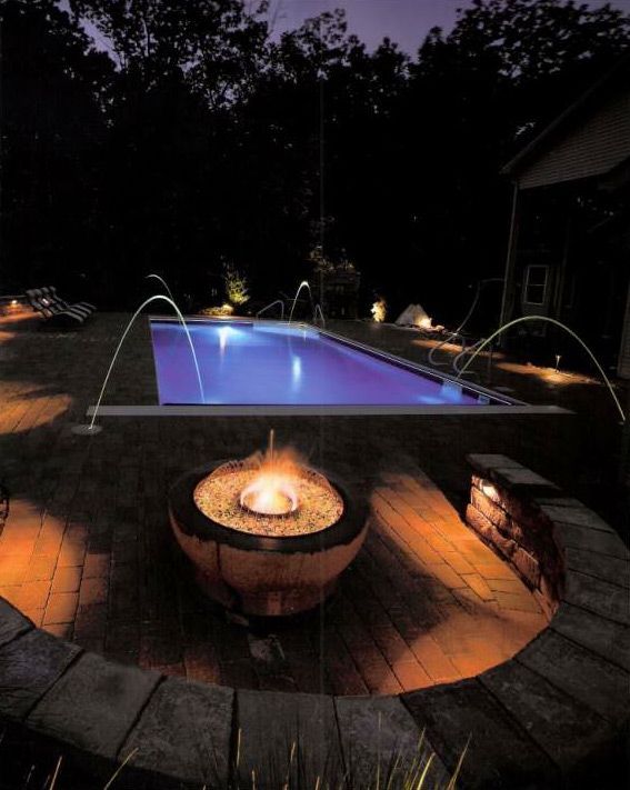 A fire pit in front of a swimming pool at night